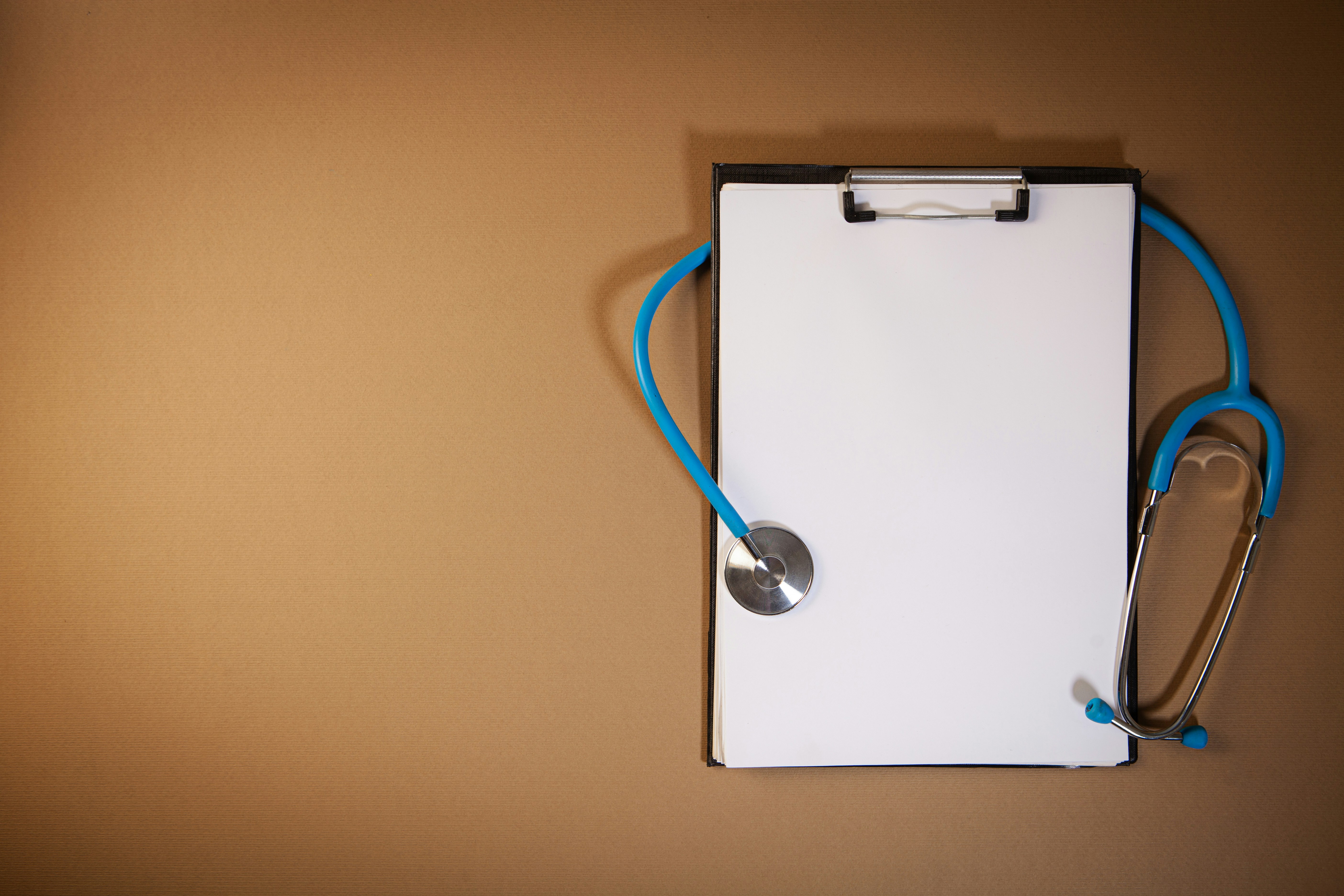 A blank paper document on a clipboard accompanied by a blue stethoscope on a brown background